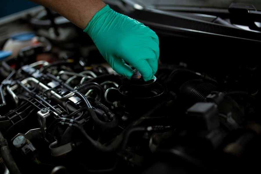 Gloved hand opening the oil filler cap on a car engine
